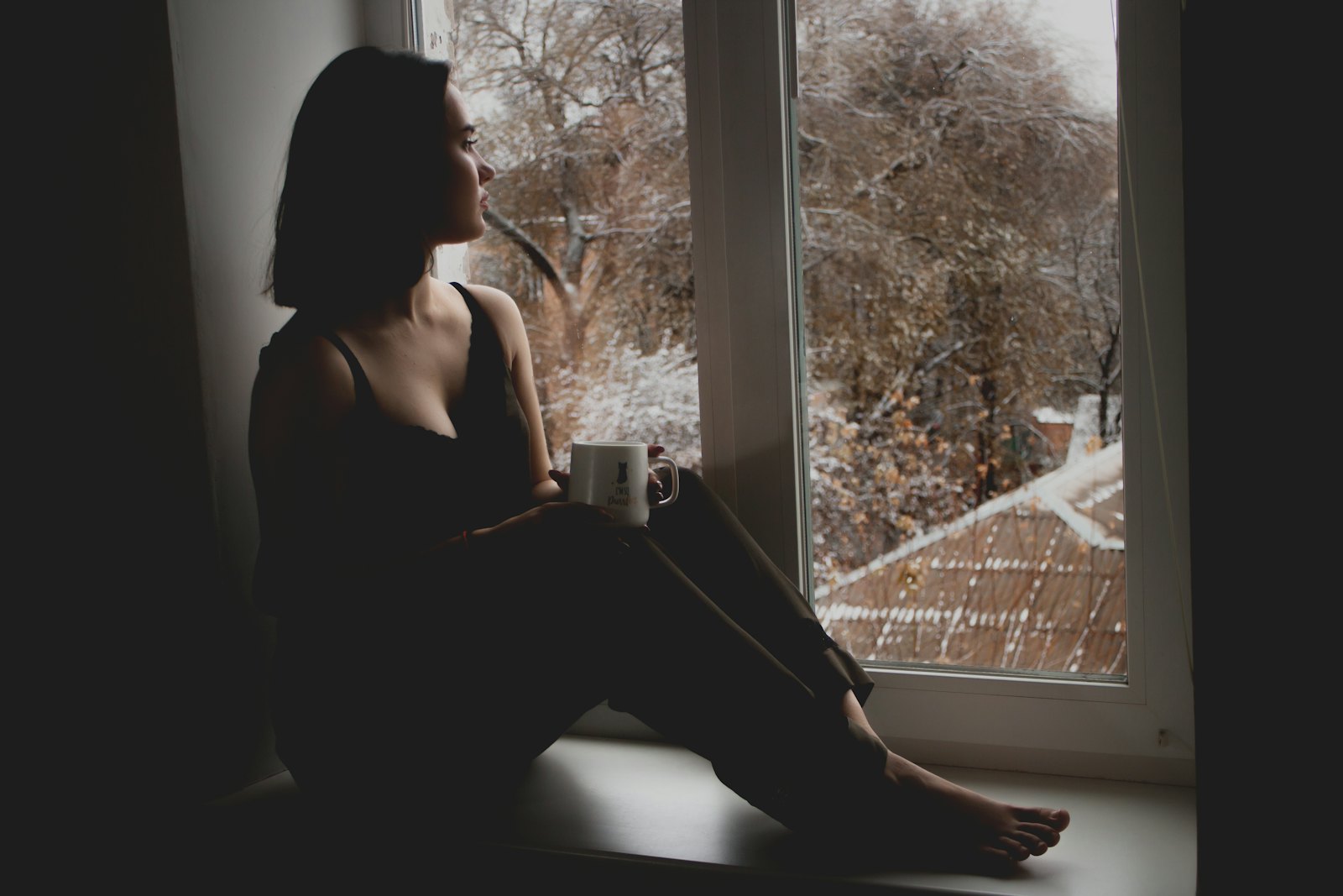 A person sitting quietly by a window with a mug, looking outside