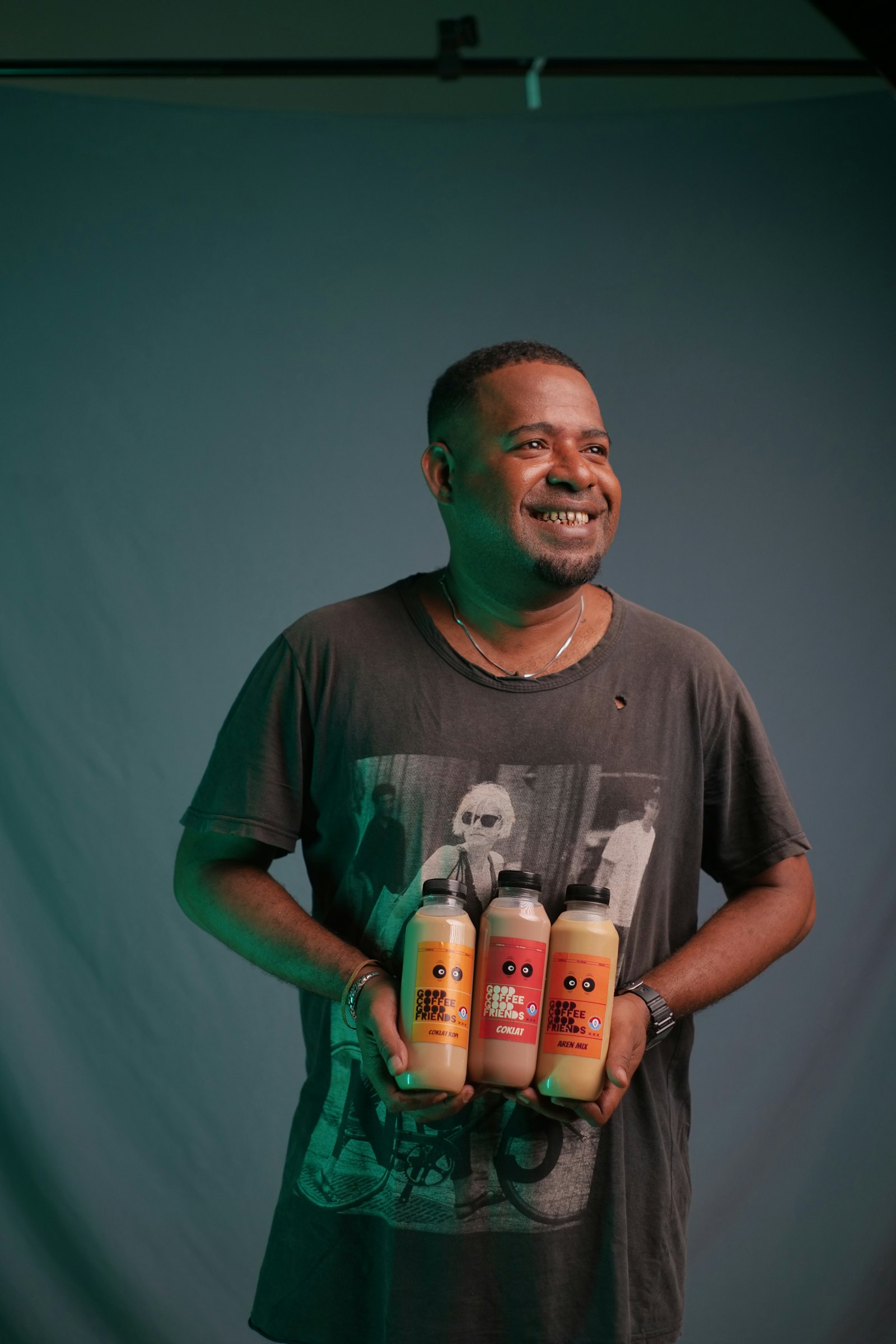 A founder smiling, holding three bottles of the drink they make