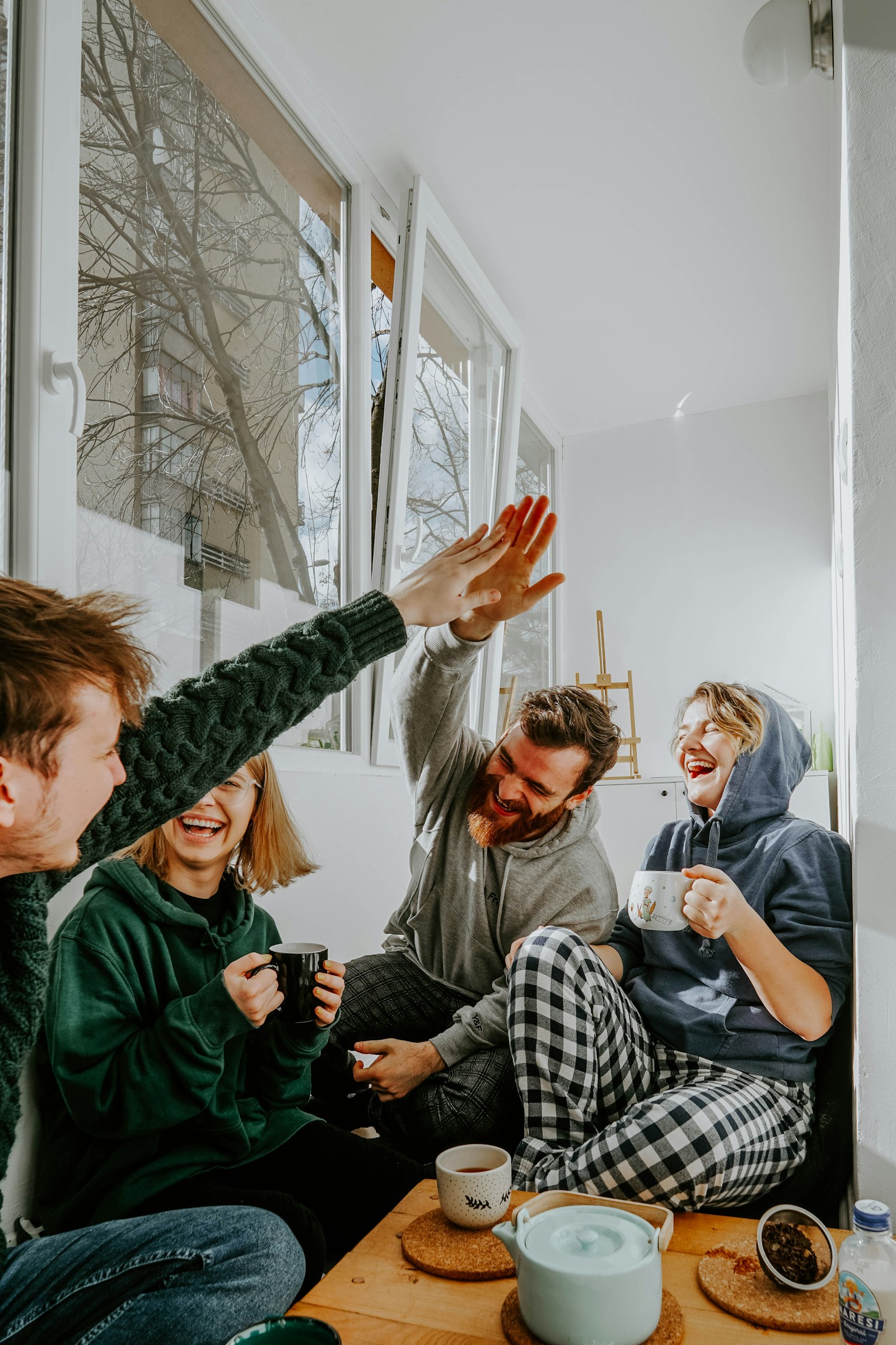 Four friends laughing together over coffee in bright daylight