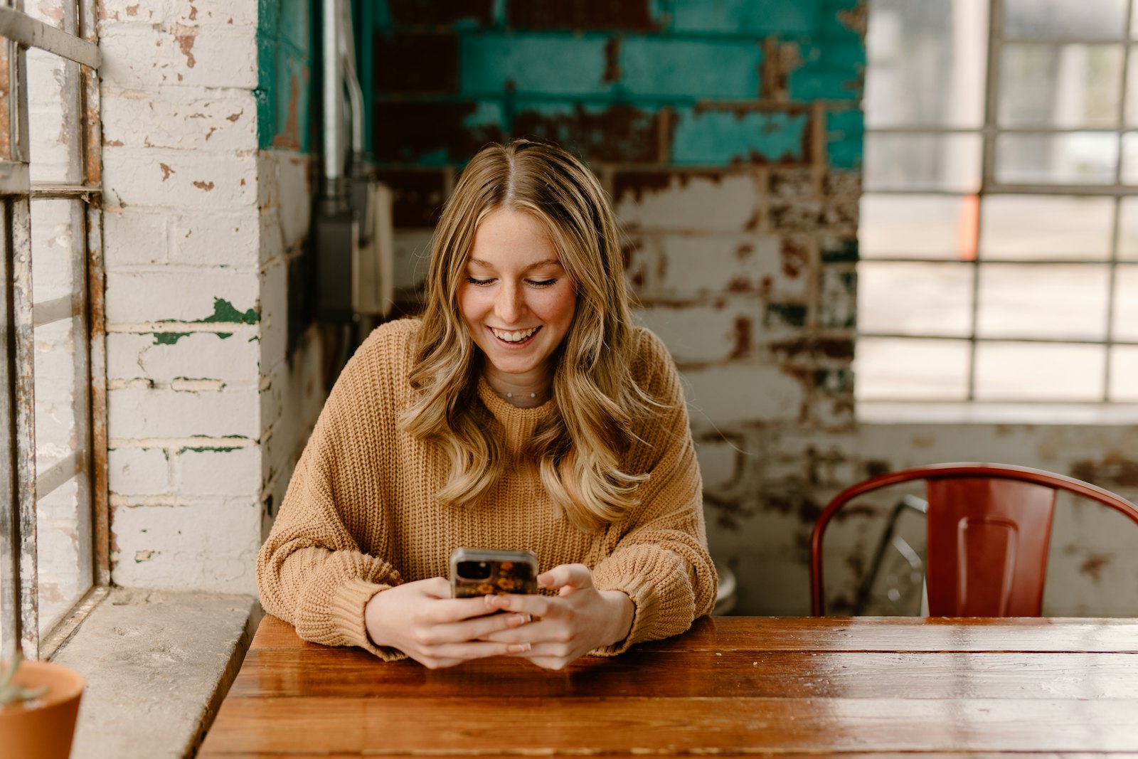 A smiling young woman scrolling her phone at a cafe table